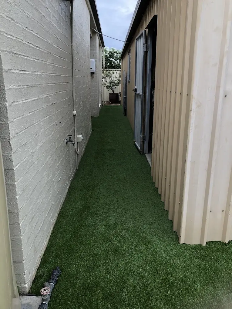 Artificial grass fitted down a narrow side passage between a brick wall and a shed